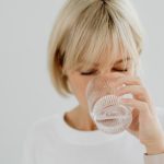 Blonde woman drinking water from glass indoors, showcasing healthy lifestyle and hydration.